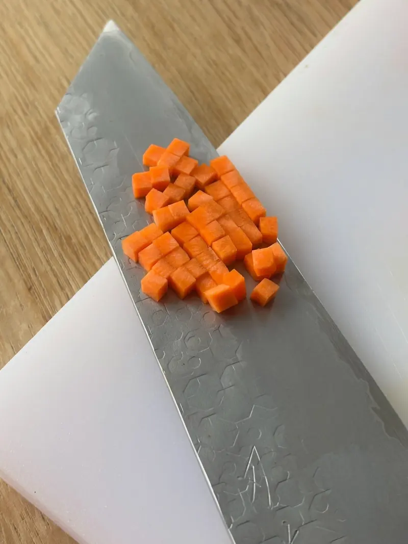 Fijn gesneden brunoise van wortel op een koksmes